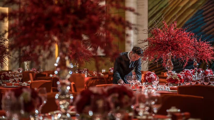 Hotel staff sets banquet tables with large red flower arrangements