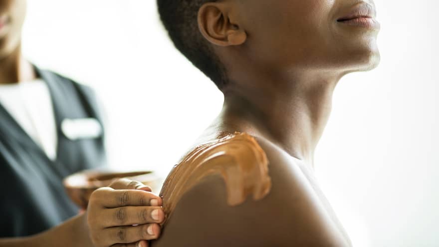 Woman's shoulder, neck and chin as spa staff rubs clay, lotion on her skin