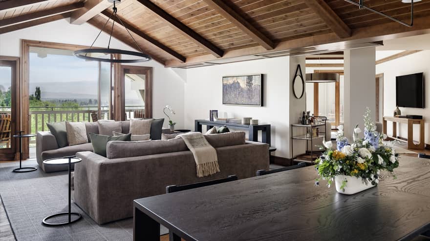 Living and dining area with vaulted wood ceiling, two grey sofas, dining table with a floral centrepiece, and mountain views