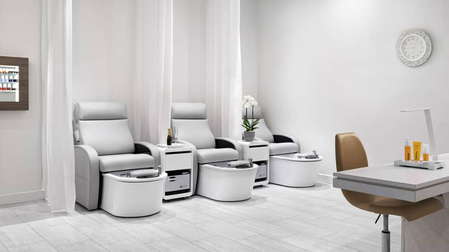 Nail salon with three light grey pedicure chairs, separate by white curtains, and one manicure station