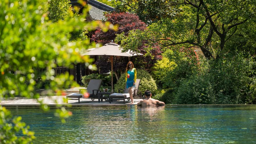 Woman in blue dress walks towards man wading in outdoor swimming pool