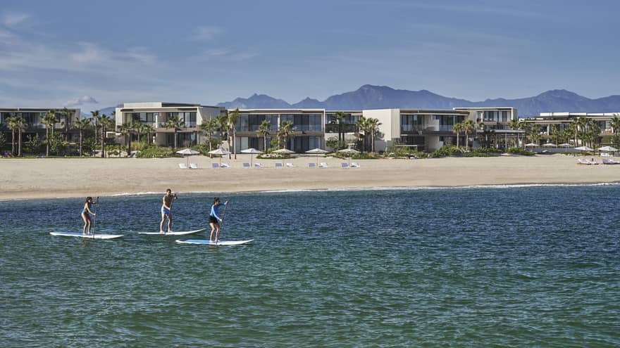 Three people on paddle boards in the water with a hotel behind them.