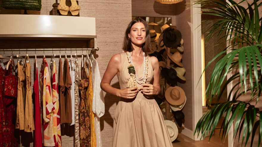 A woman in trendy resort boutique wears beige-coloured dress and Hawaiian necklace