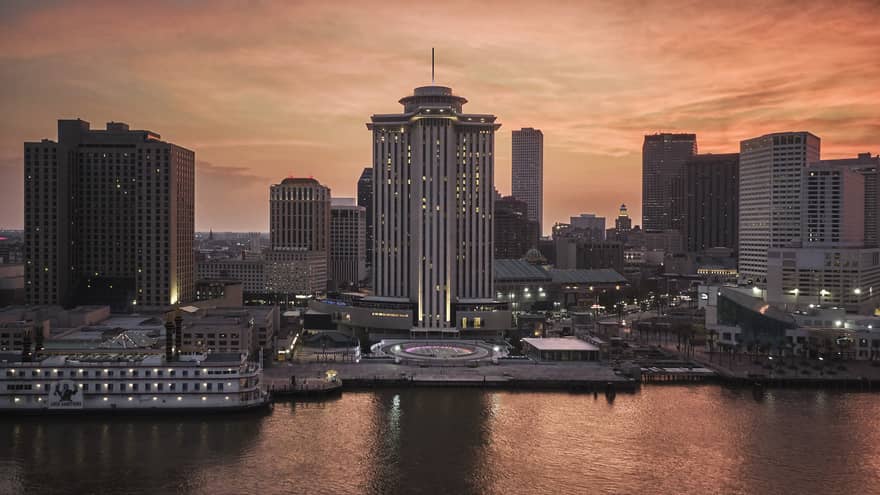 The exterior of a tall building next to a body of water with a city in the background.