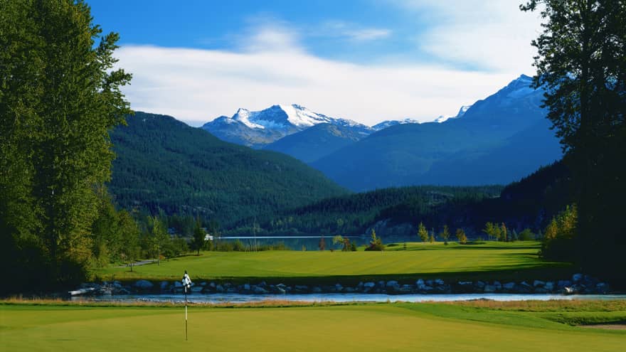 Big Sky Golf Course green, flag in front of pond, snow-capped mountains in background