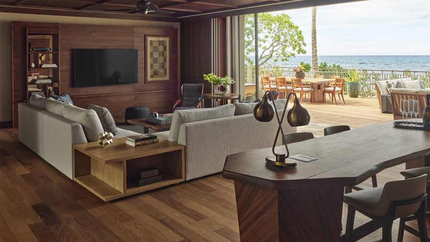 Wooden desk and living room with light grey sofa, full wall of windows with ocean view