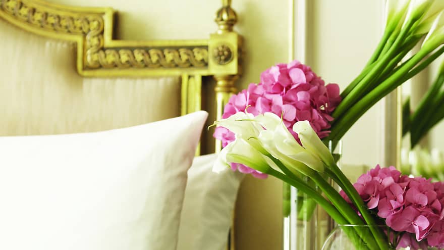 Close-up of white pillows against silk headboard with gold frame, fresh purple and white flowers