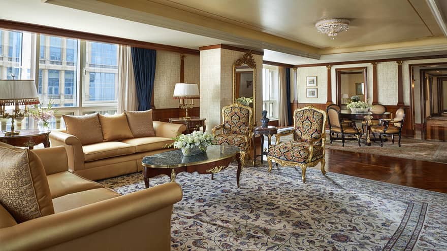 Royal Suite living room with two gold sofas, antique-style armchairs on large area rug, dining room in background