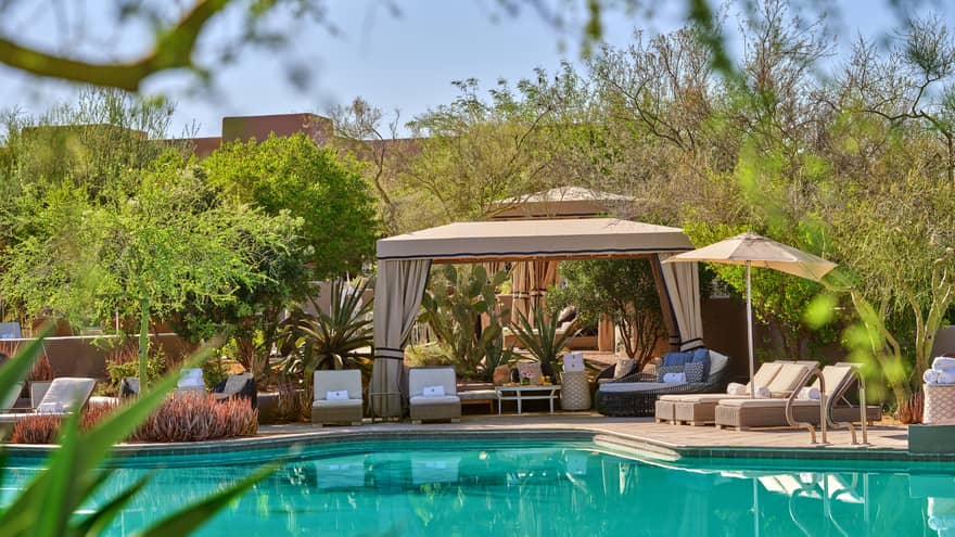 Blue pool with cabana and lounge chairs, surrounded by trees and greenery.