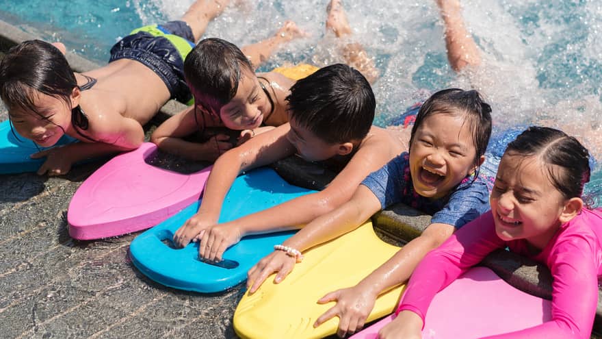 Lineup of smiling children with boogie boards splashing in the pool