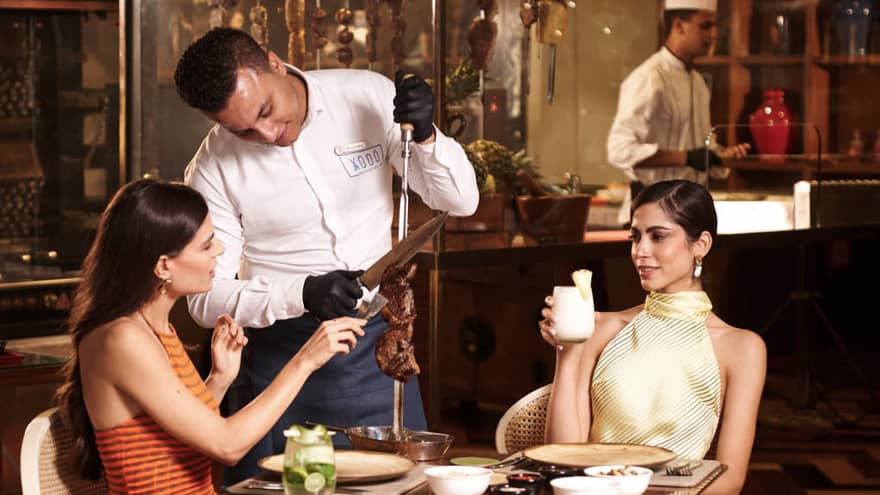 Two people at restaurant are served churrascaria off carving spit from chef