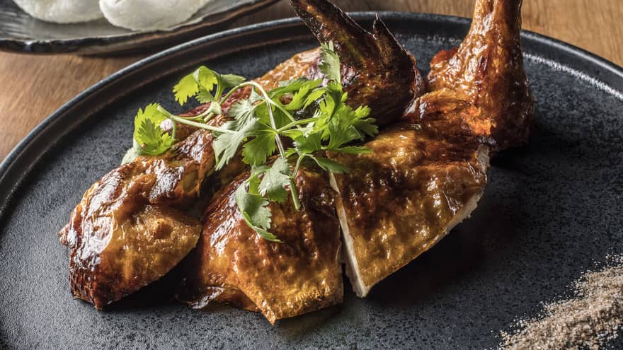 Half chicken on dark plate with coriander garnish 
