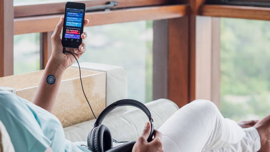 Person resting on spa lounger holding a device in left hand corded to headphones on lap