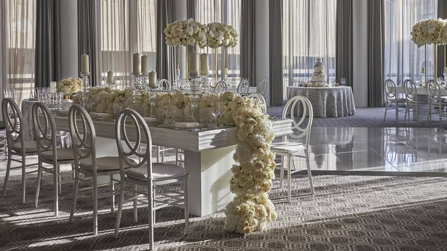 Long white rose garland over small dining table in bright banquet room