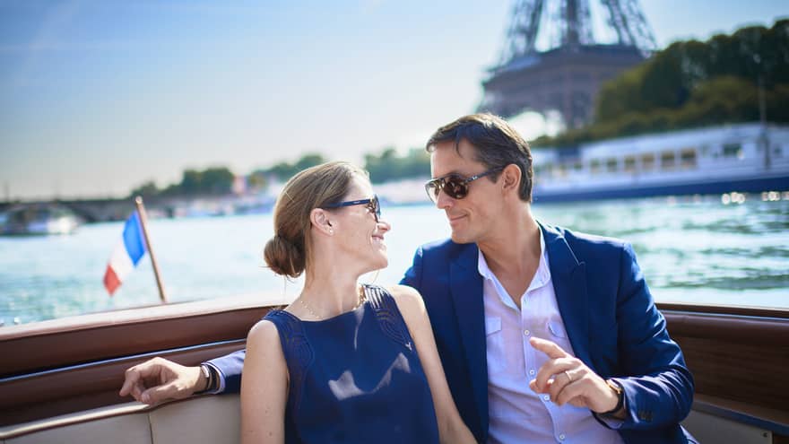 Couple enjoy Paris boat ride next to small France flag, Eiffel tower in background