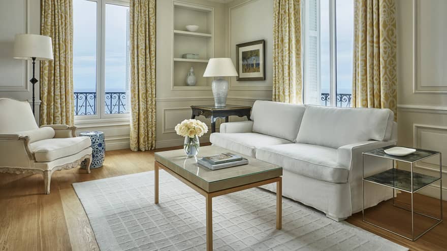 Modern white sofa, armchair, rug, table with books, flowers, corner windows