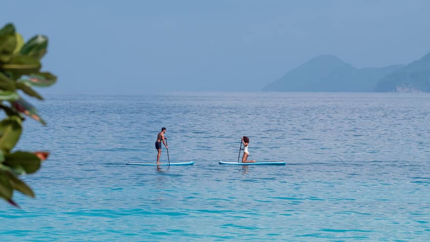 Man and woman paddle board on the open ocean, mountains visible through the fog