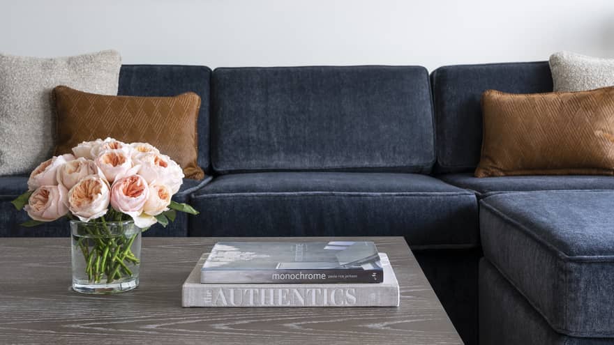 A blue couch near a grey coffee table with books and flowers on it.