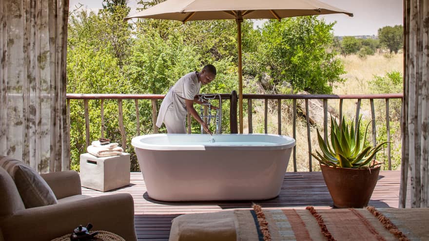 Woman draws bath in freestanding tub on patio beside large cactus plant in pot
