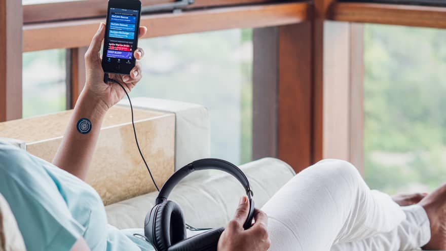 Person resting on spa lounger holding a device in left hand corded to headphones on lap