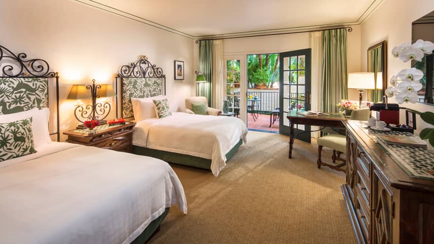 Double beds across from large wood dresser, TV, white orchids, open balcony door