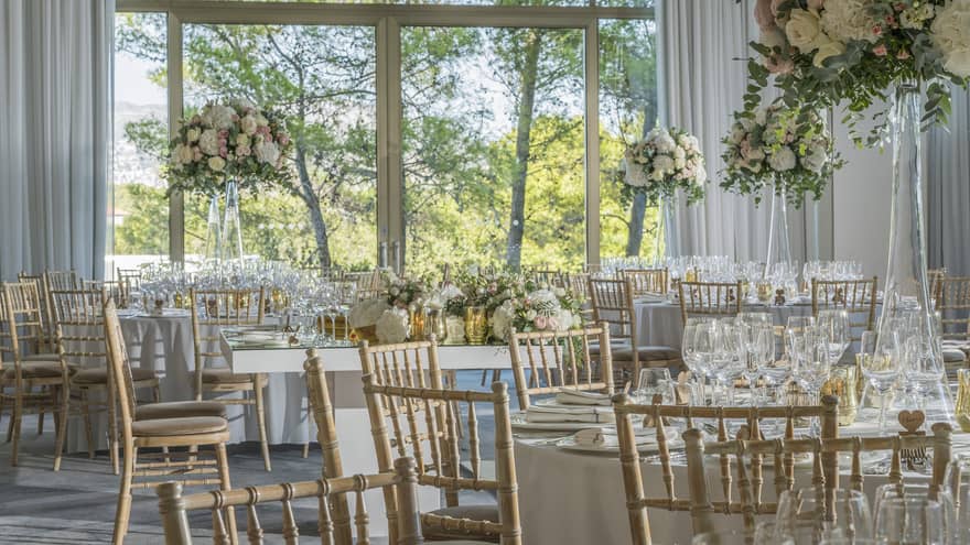 Wedding banquet tables with pink roses in tall vases in event room with floor to ceiling windows