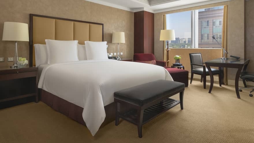 Hotel room with king bed, tan headboard, bench, table and two chairs and window-side chaise