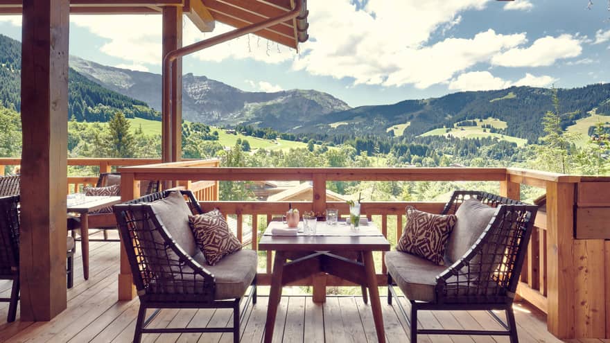 Two cushioned benches with table in middle on wooden terrace with mountain views