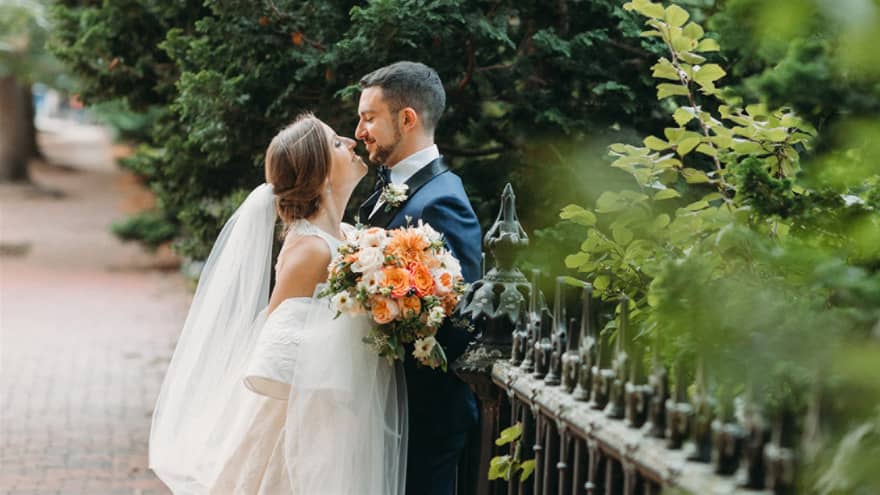 A bride and groom embrace on a city street surrounded by trees