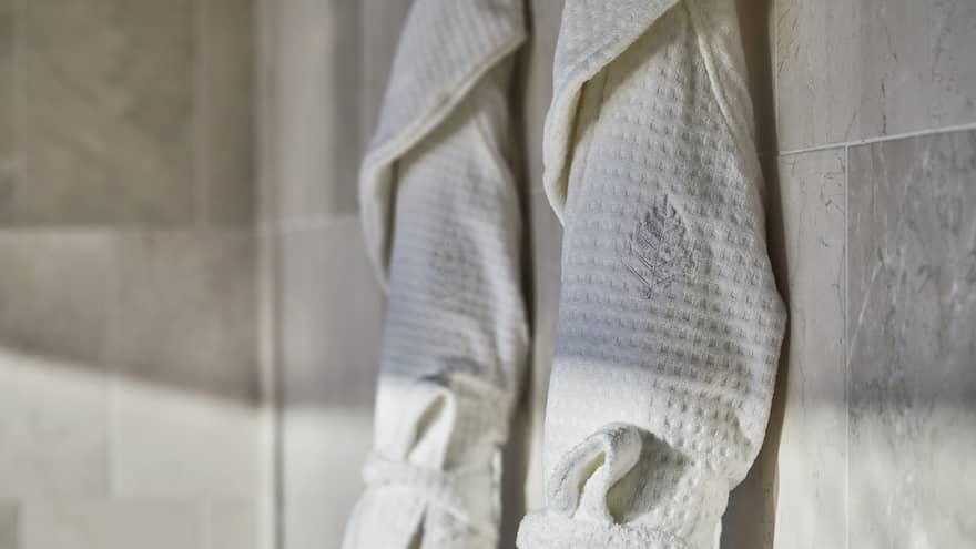 Two spa robes hanging on a wall of smooth tile.