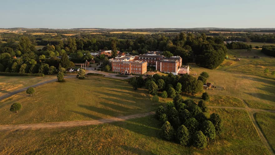 A bird's-eye view of a large building nestled among fields and wooded areas
