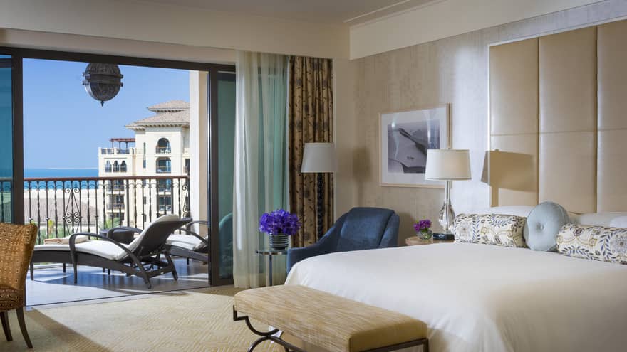 Imperial Suite bed with tall padded headboard, blue accent chair and open glass doors to patio