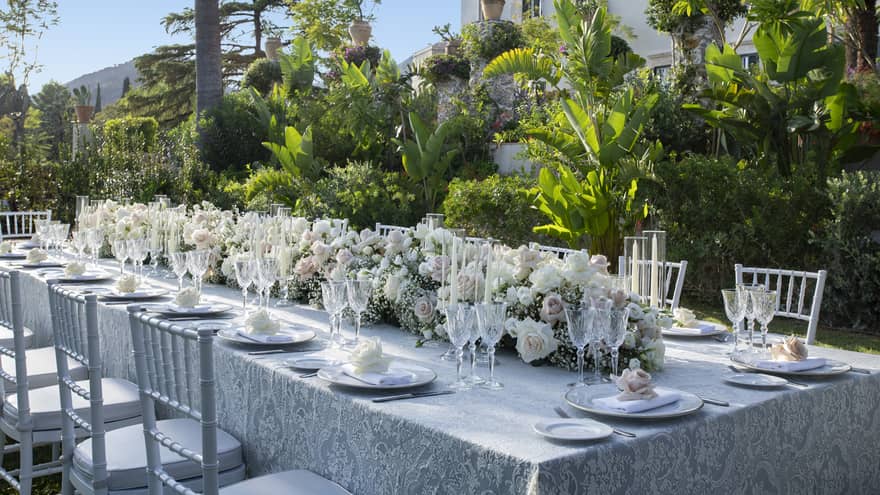Elegantly set long table with extended floral wedding centrepiece alongside lush garden wall