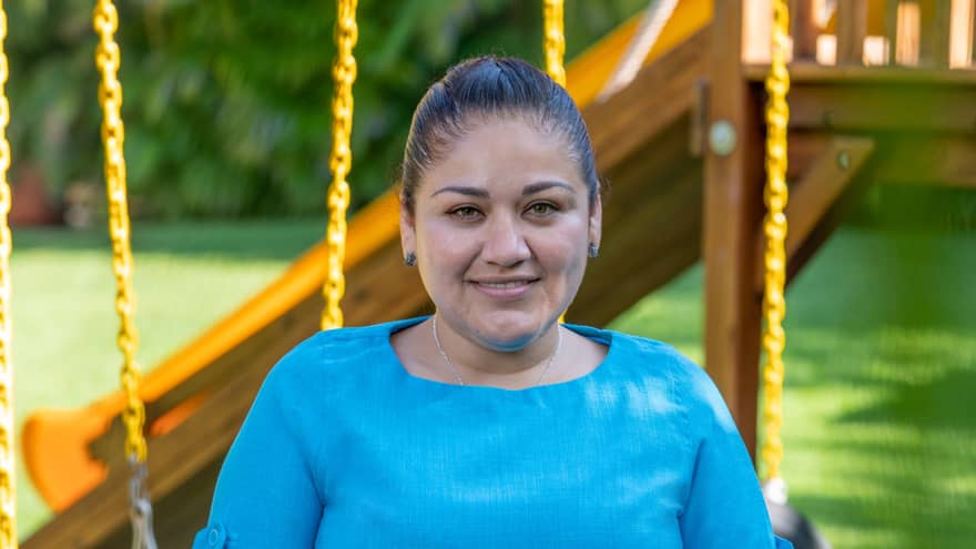 A woman in a blue shirt outside near a playground.
