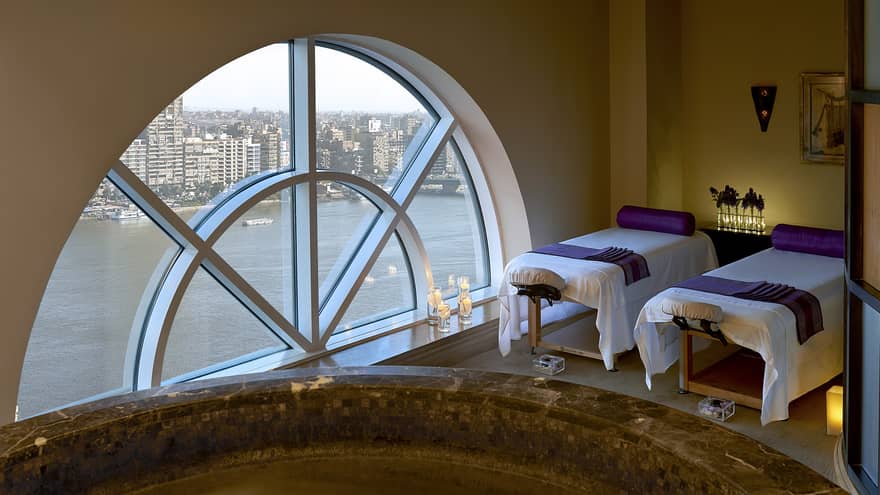 Two massage tables side-by-side in couples spa suite by lare crescent-shaped window overlooking Nile