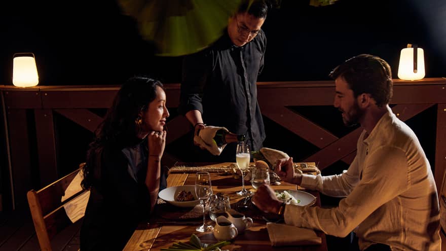 An elegant couple sharing an intimate dinner at a beautifully set table, while a graceful waiter pours champagne into their glasses