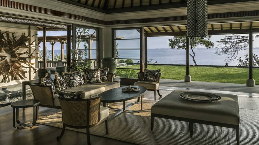 Imperial Villa open-air living room with elegant wicker sofa, chairs, large ottoman table with platter, green lawn overlooking ocean