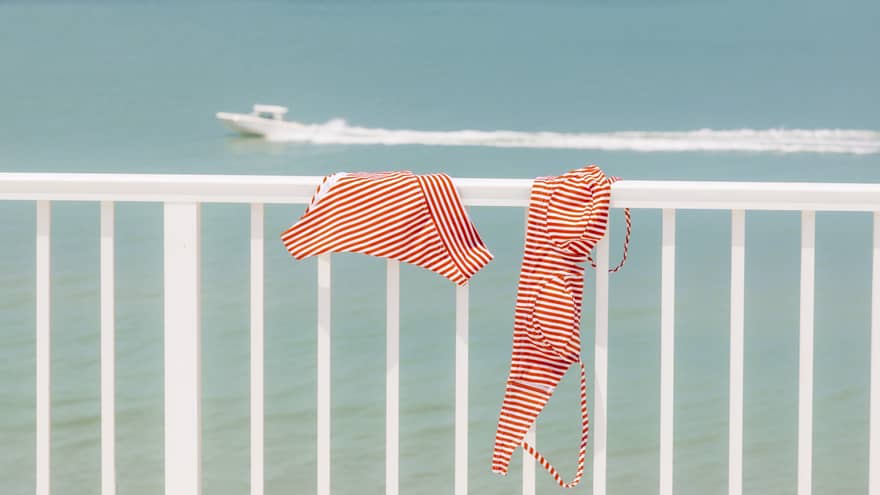 Red-and-white-striped bikini hangs on a white balcony railing overlooking the ocean