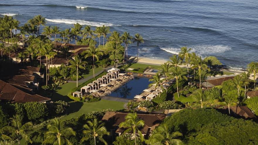 Tropical resort pool lined with cabanas and palm trees, next to the beach and ocean