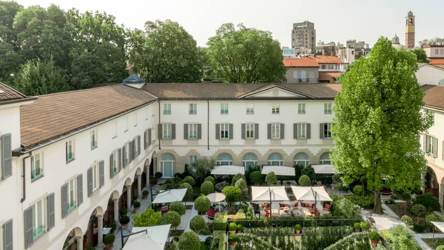 Aerial view of a hotel courtyard, featuring a lush garden, outdoor dining areas and a historic building with arched walkways
