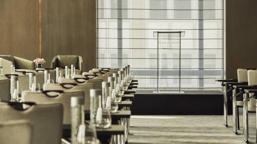 Glass podium beyond rows of meeting tables and chairs in Greenwich Ballroom