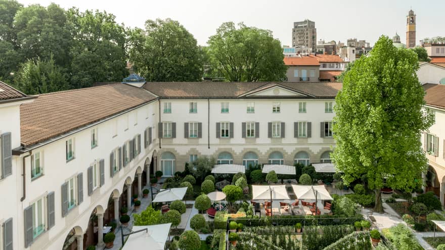 Aerial view of a hotel courtyard, featuring a lush garden, outdoor dining areas and a historic building with arched walkways