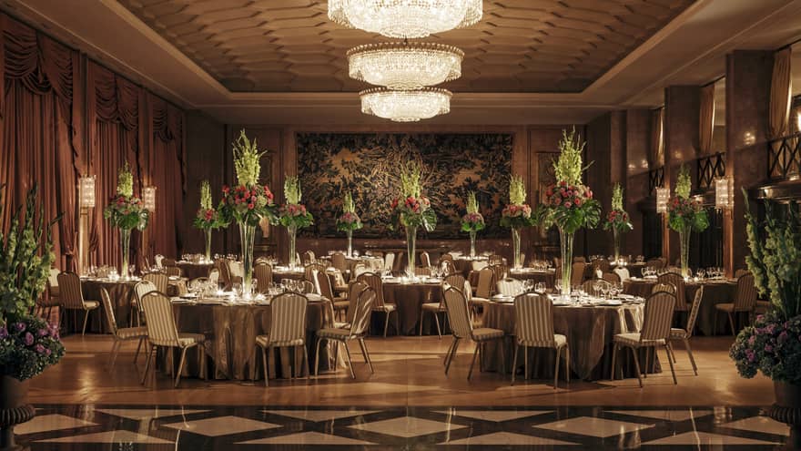 Art Deco-style dining room with tiles, banquet tables with tall flower arrangements, crystal chandelier 