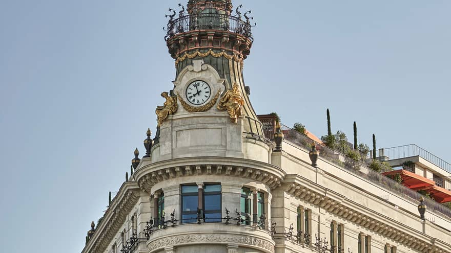 Historic ornate building with a clock tower, decorative ironwork and rooftop garden, featuring detailed stonework and balconies