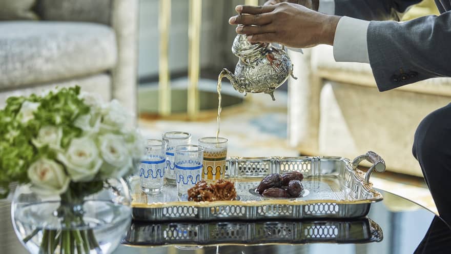 Table with roses, staff pouring tea into decorative glass cups on tray with dates