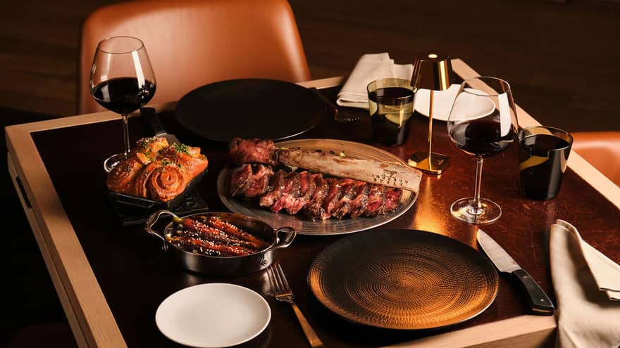  A dining table with wine glasses, culinary dishes and utensils beside plates