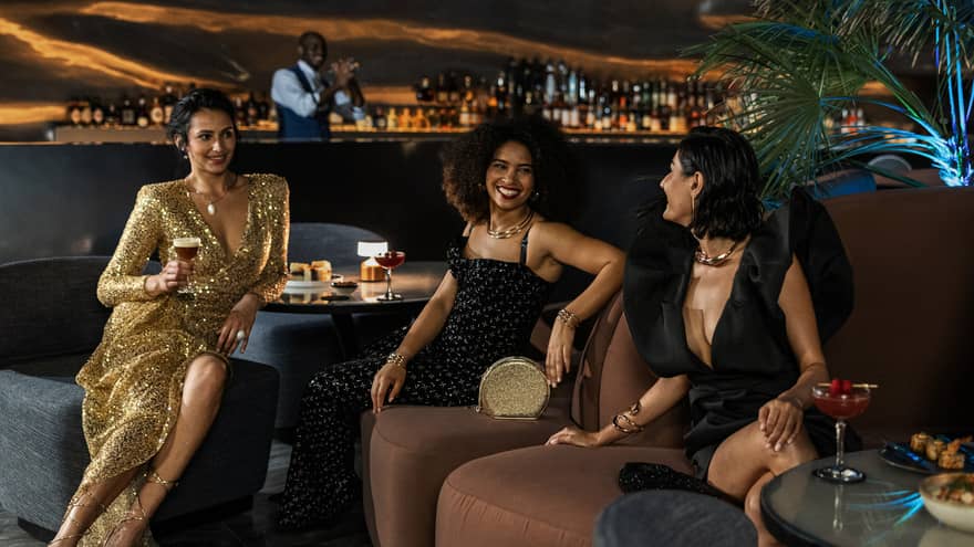 Three women and one man mingle over cocktails at Dubai hotel rooftop lounge