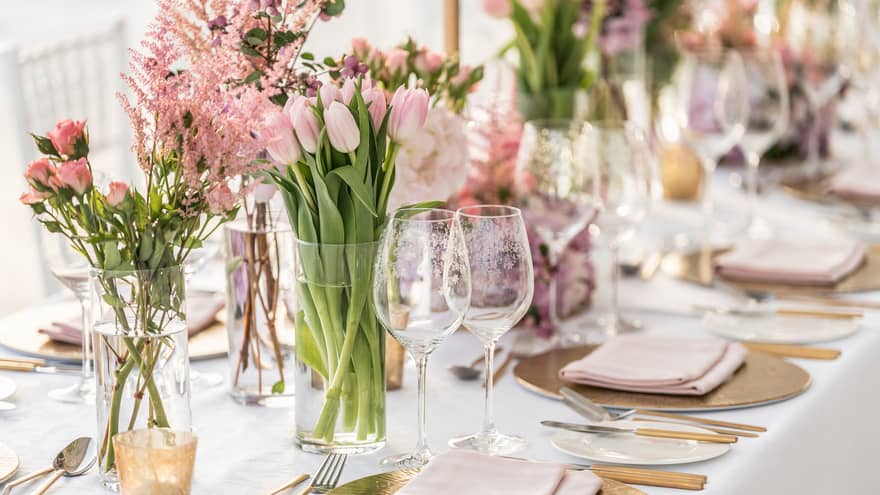 A banquet table is decorated with gold chargers, pale pink linens and a variety of pink florals