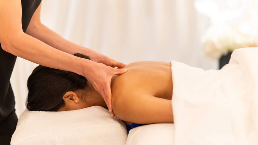 Spa therapist massaging shoulders of guest lying facedown on white spa table