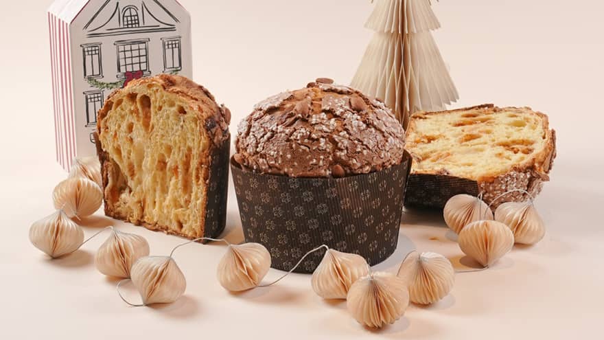 One whole panetonne and one sliced in half set on a white backdrop next to paper holiday decorations